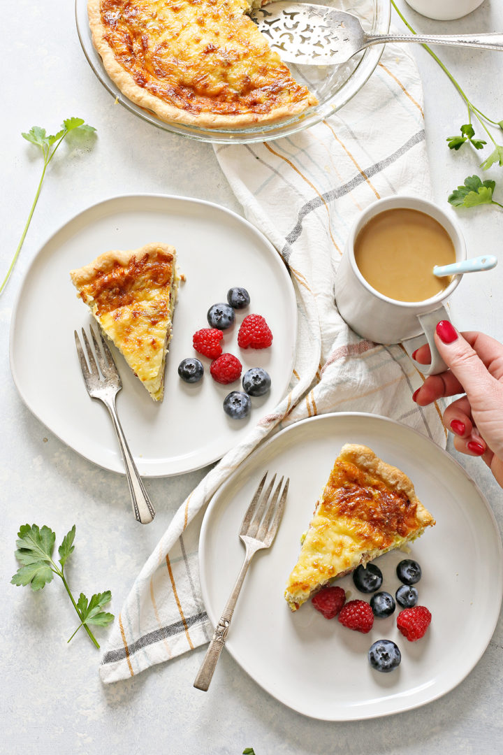 woman picking up a cup of coffee off of a brunch table that is set with plates of quiche lorraine