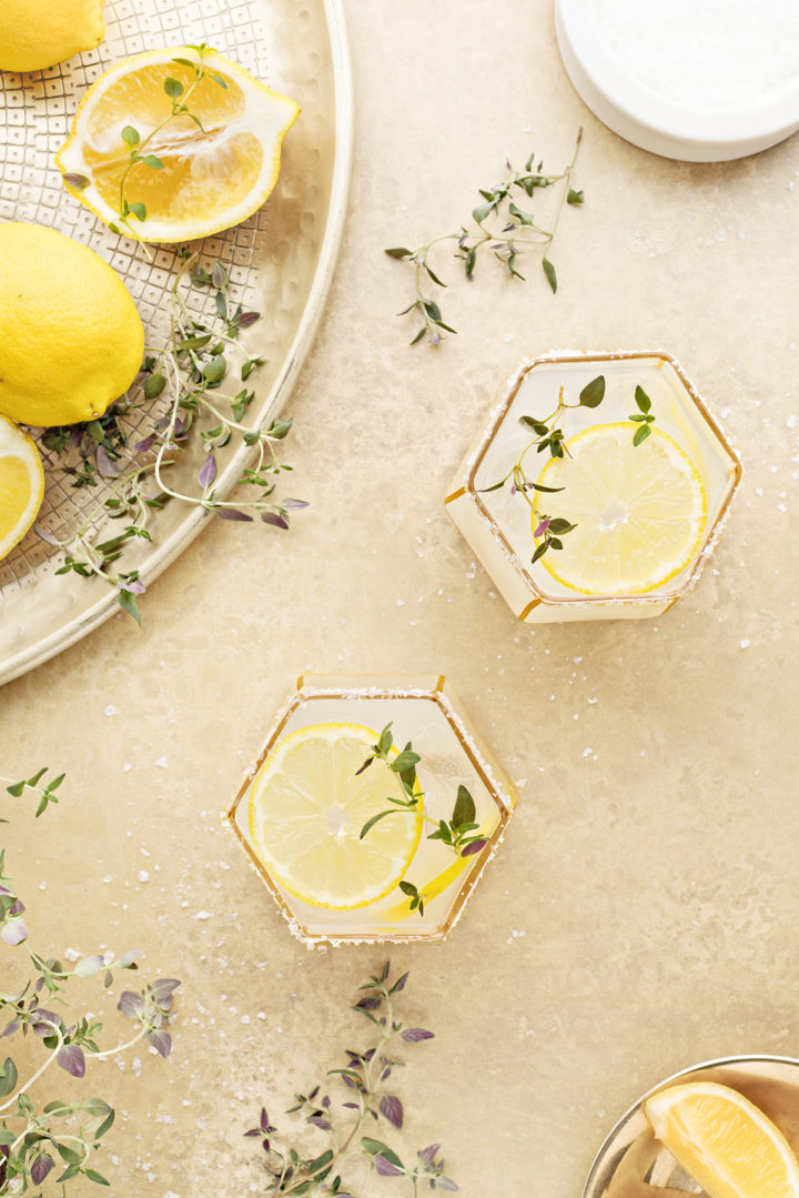 overhead photo of two lemon margaritas on a gold background with fresh thyme and lemon