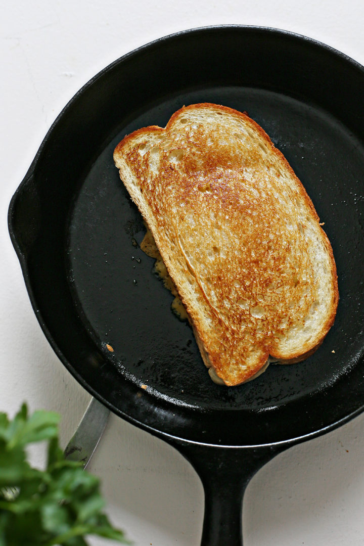 a grilled cheese and bacon sandwich cooking in a cast iron skillet