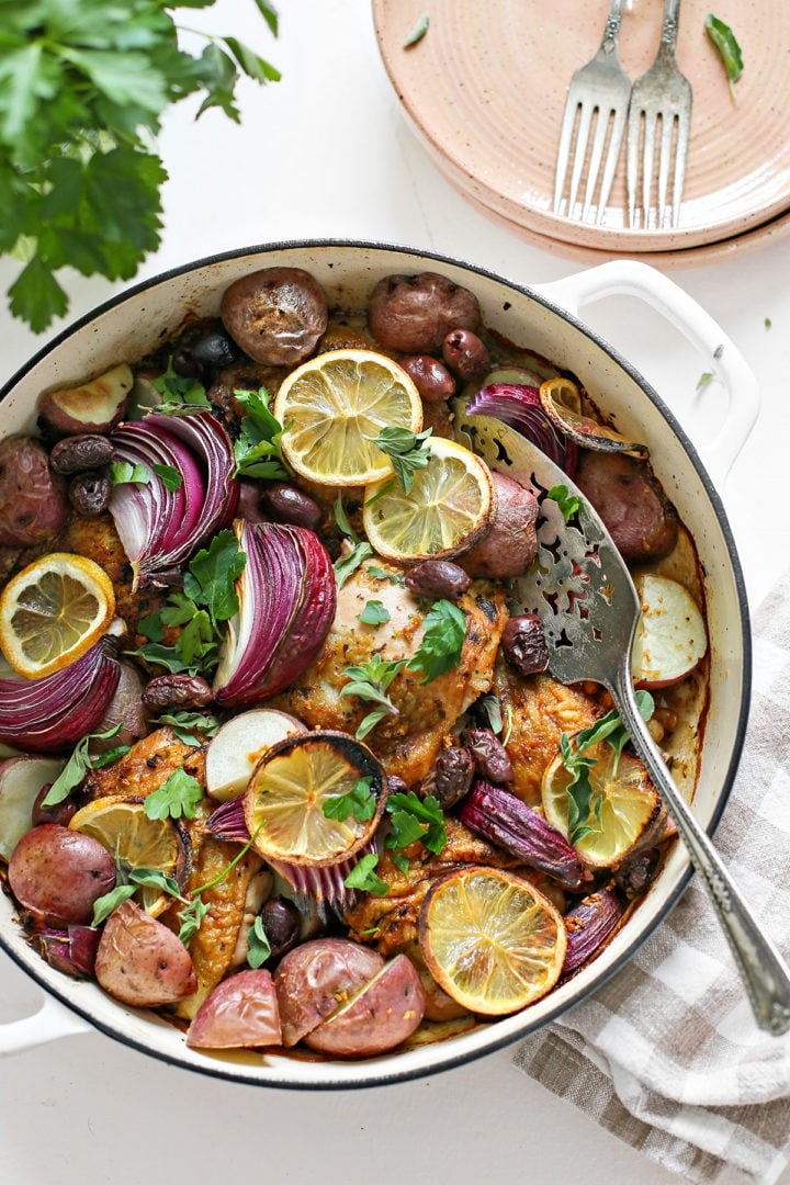 a white cast iron pan with a baked chicken thigh recipe in it, set on a table with plates ready to serve