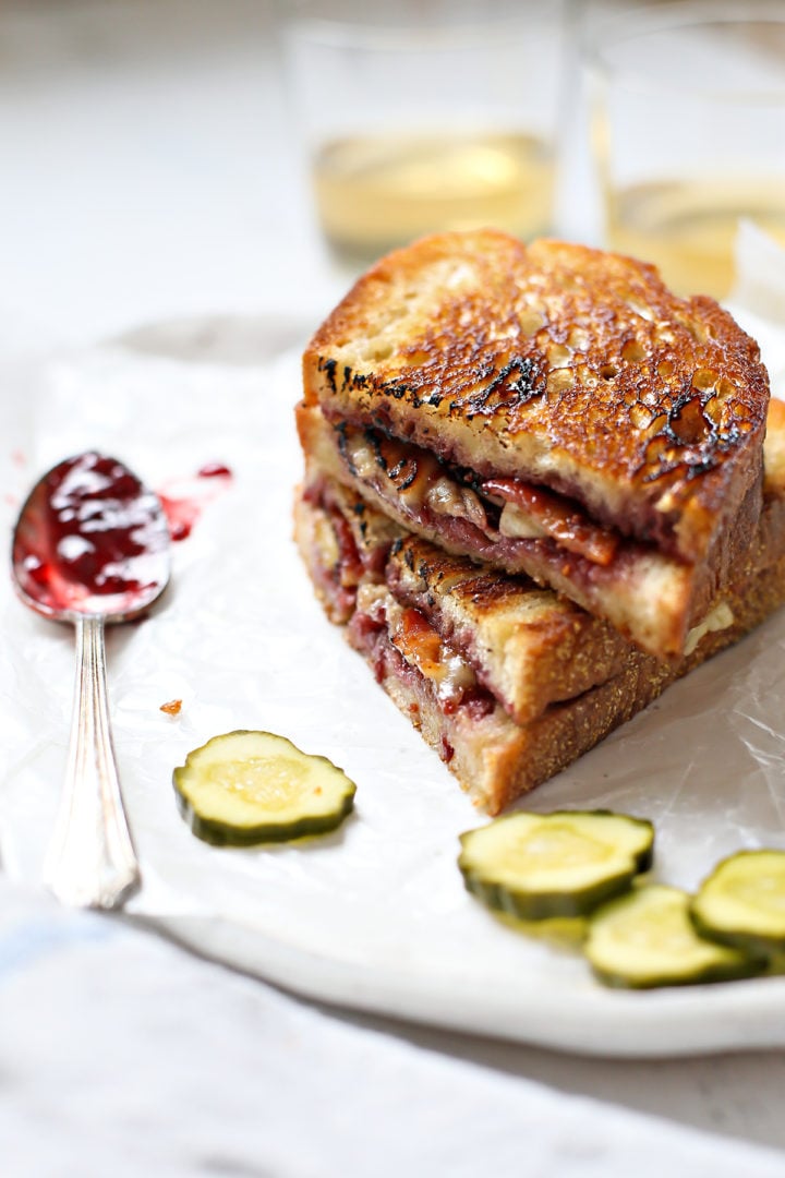 two slices of a brie grilled cheese stacked on top of each other next to pickle slices