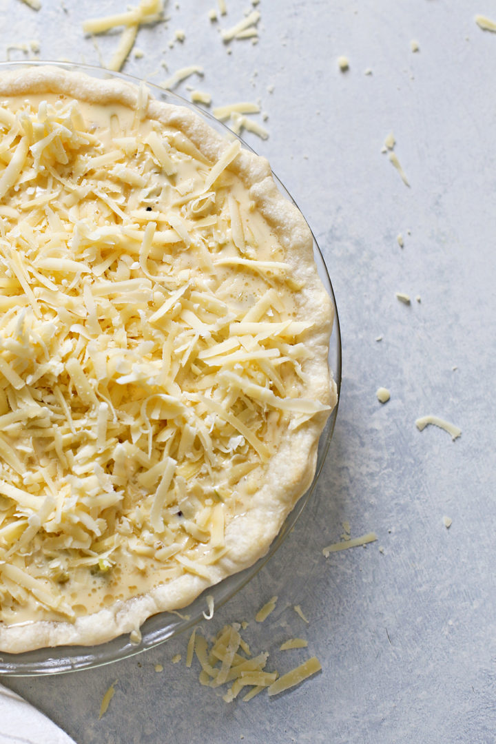 photo of an unbaked lorraine quiche with gruyere cheese on top ready to go in the oven