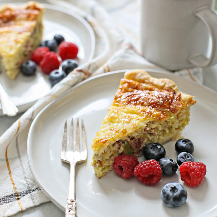 a table set with two plates of quiche lorraine, fresh berries, and a cup of coffee