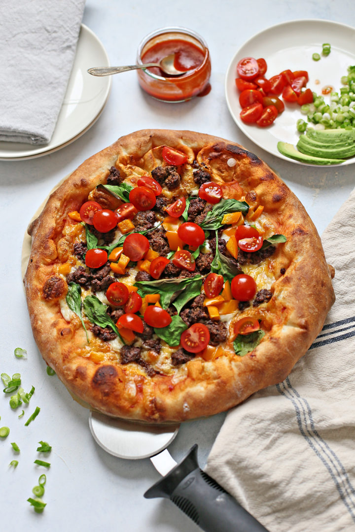 a cooked taco pizza on a light background with a pizza cutter