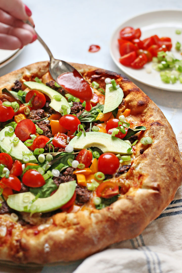 woman adding hot sauce onto a taco pizza