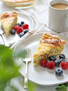 a table set with two plates of quiche lorraine, fresh berries, and a cup of coffee