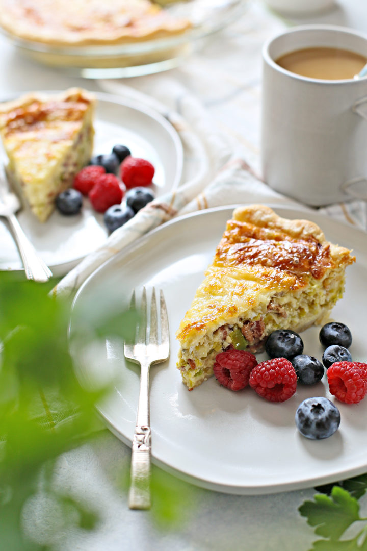 a brunch table set with two plates of quiche, fresh berries, and a cup of coffee