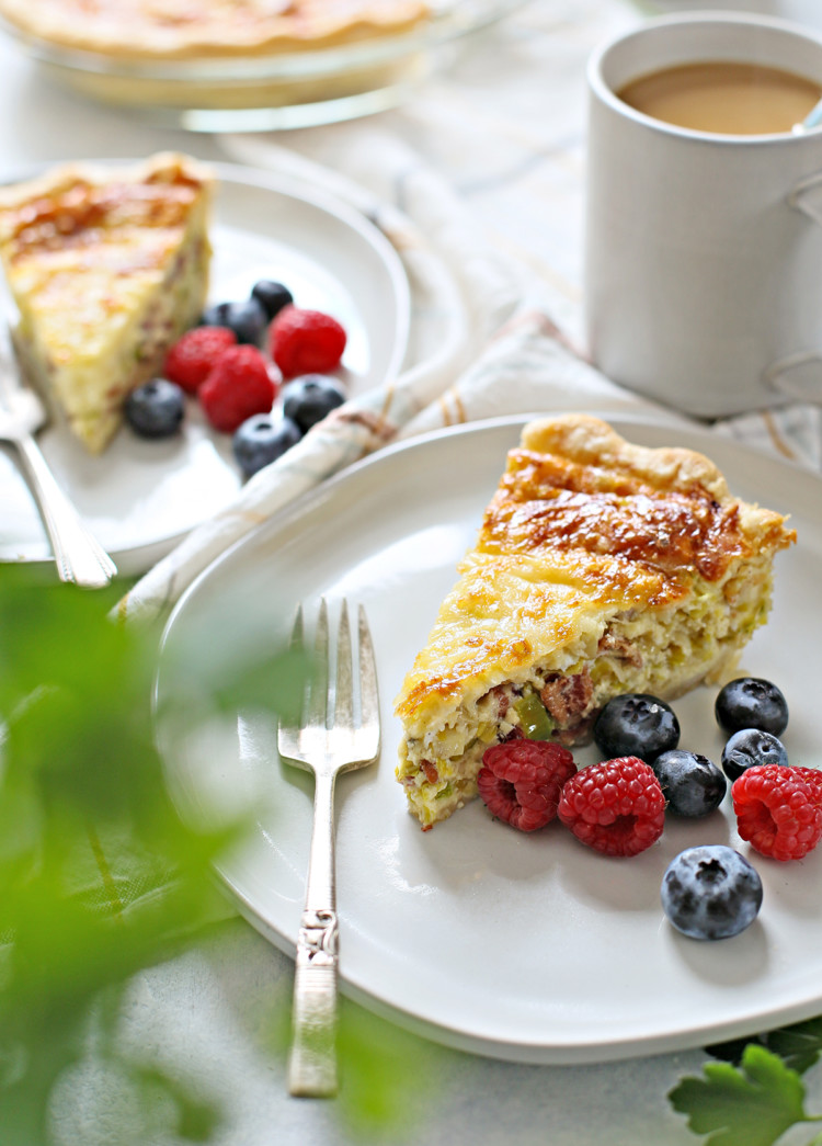 a table set with two plates of quiche lorraine, fresh berries, and a cup of coffee