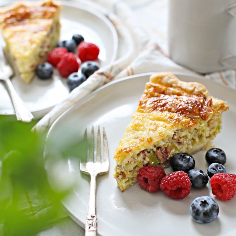 a table set with two plates of quiche lorraine, fresh berries, and a cup of coffee