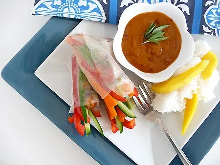 a square white plate with a serving of coconut rice and mango with Vietnamese shrimp rolls and a bowl of spicy peanut dipping sauce