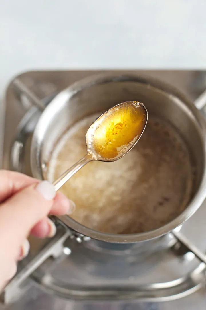 woman holding a spoonful of browned butter to show the milk solids and golden color