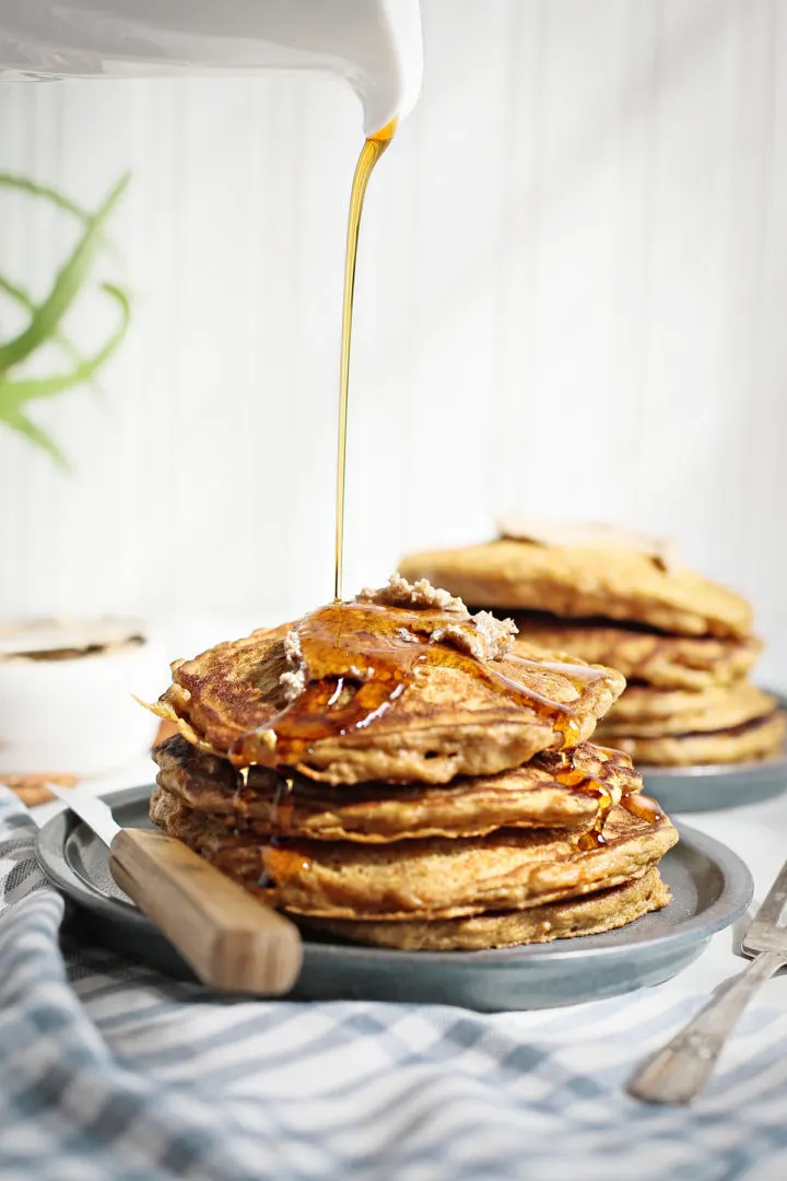 Easy Carrot Cake Pancakes with White Chocolate Pecan Butter maple syrup pouring on top of a stack of carrot cake pancakes