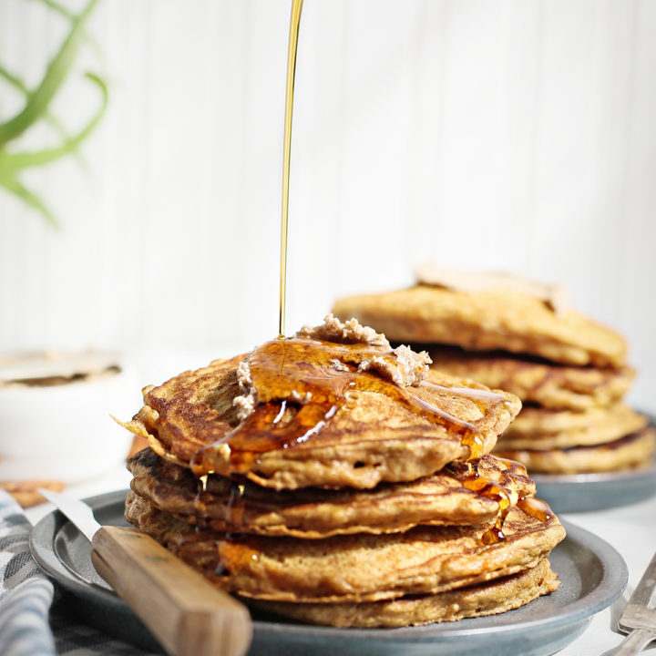 maple syrup pouring onto a stack of carrot pancakes on a dark blue plate