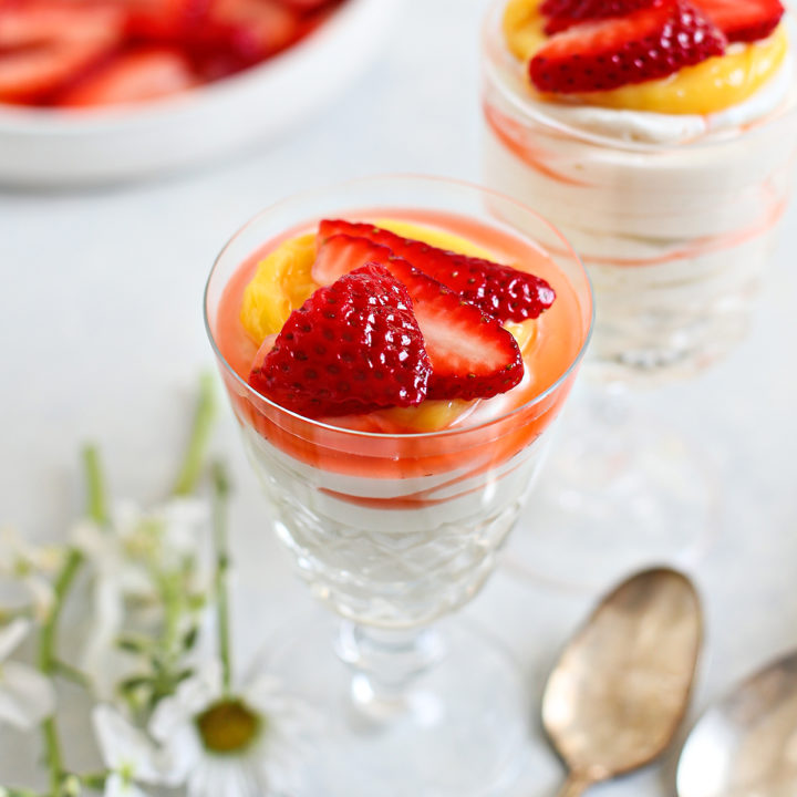 two spoons with two dessert dishes of cheesecake mousse topped with lemon curd and fresh strawberries