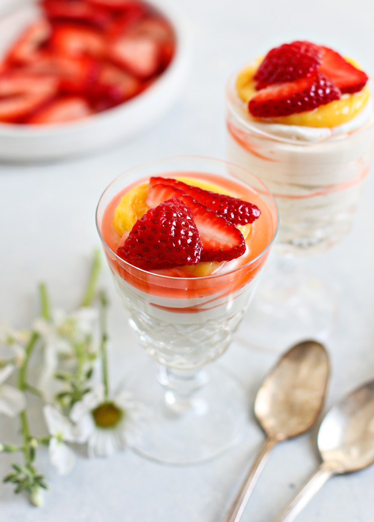 two spoons with two dessert dishes of cheesecake mousse topped with lemon curd and fresh strawberries