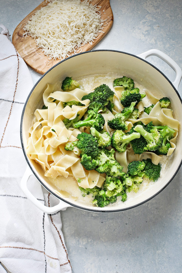 adding broccoli to alfredo sauce with pasta