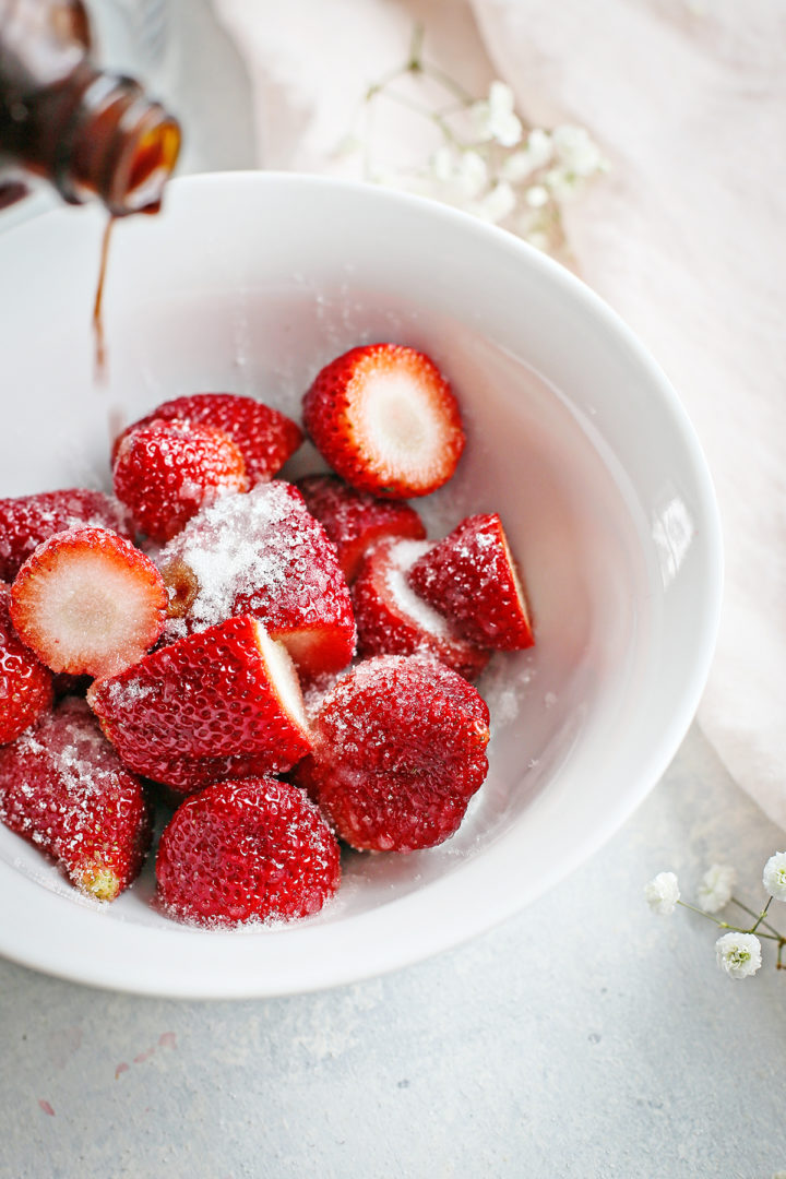 vanilla extract being added to a bowl of strawberries and sugar for this strawberry and cream dessert