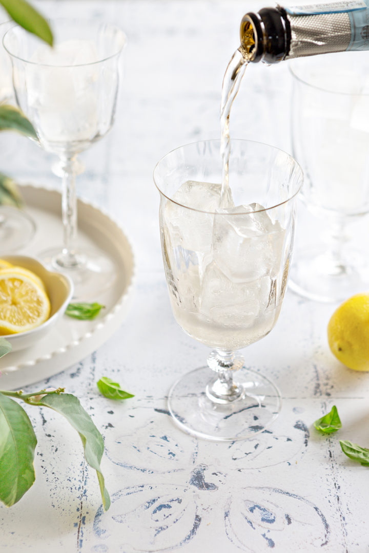hand pouring prosecco into a glass filled with ice, preparing a refreshing limoncello spritz with prosecco  