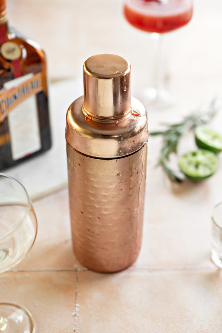 a rose gold cocktail shaker with a raspberry cosmo cocktail inside