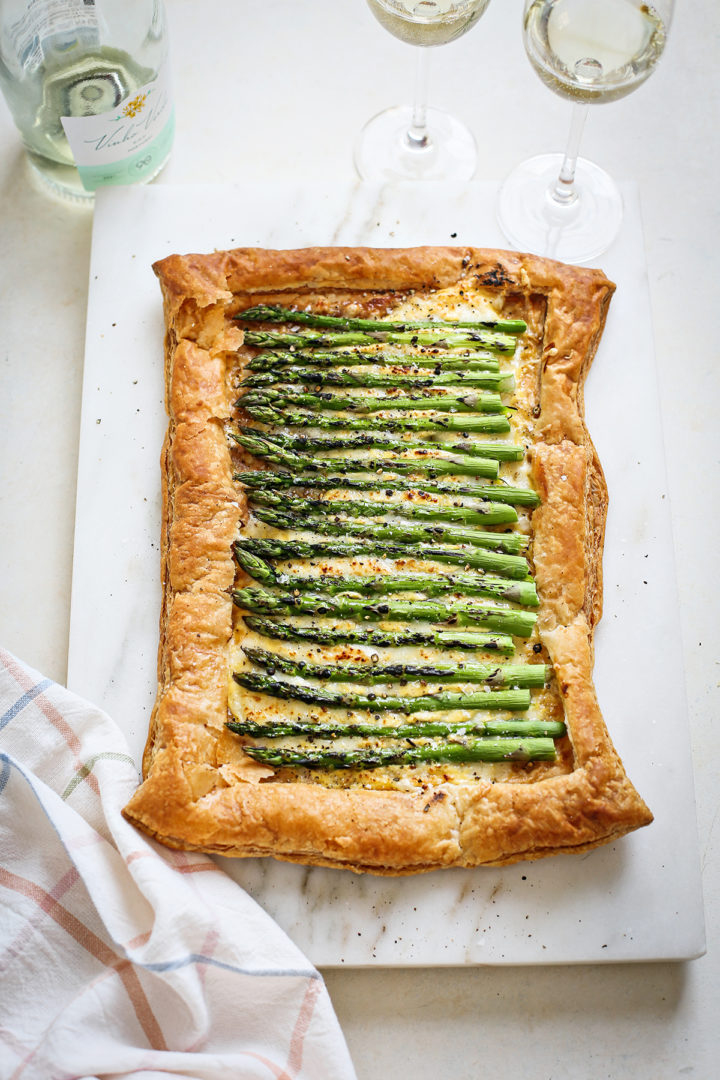 baked asparagus tart with gruyere on a marble cutting board next to a bottle of wine