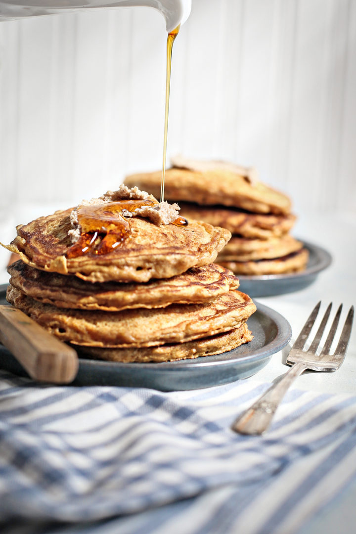 close up of maple syrup pouring onto a stack of carrot pancakes on a blue plate