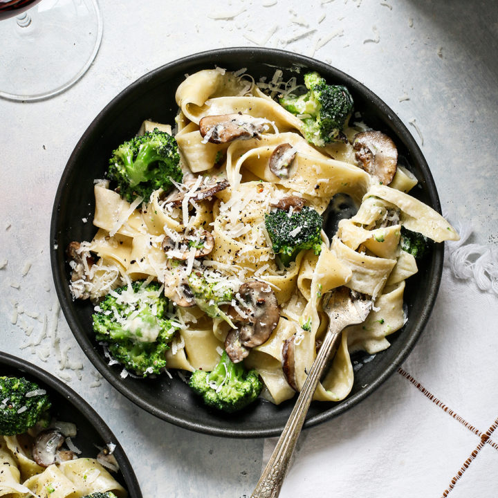 two pasta bowls with mushroom alfredo next to a glass of wine