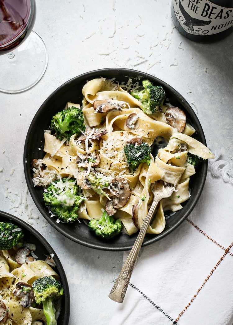 two pasta bowls with mushroom alfredo next to a glass of wine