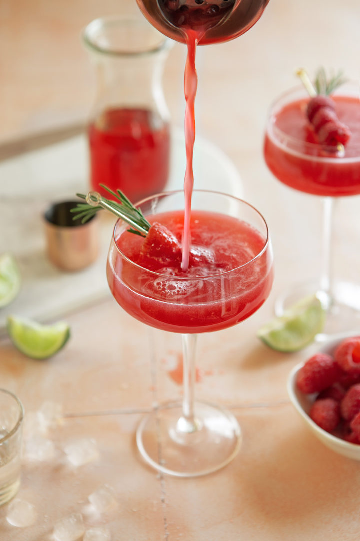 pouring a raspberry cosmopolitan cocktail into a martini glass