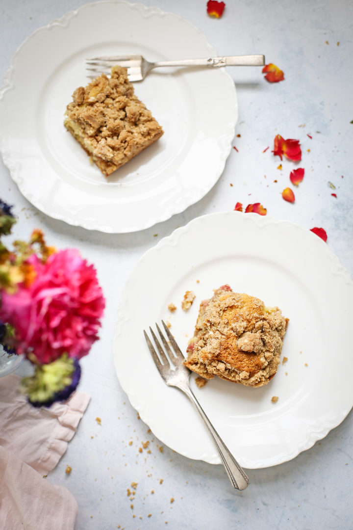 slices of rhubarb coffee cake served on two white plates on a table with flowers