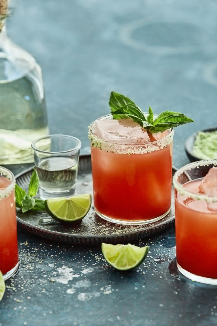 3 strawberry basil margaritas on a teal background with fresh limes and basil sprigs