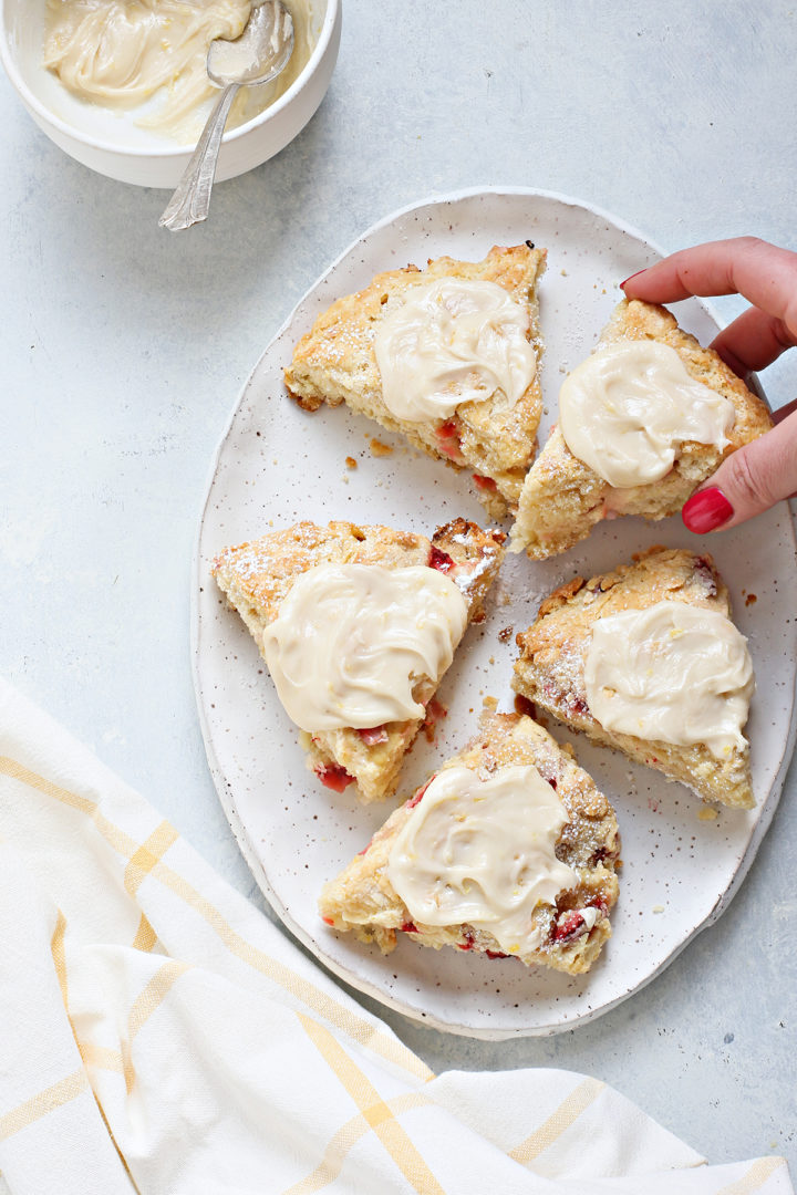 woman picking up a homemade strawberry scone with lemon glaze