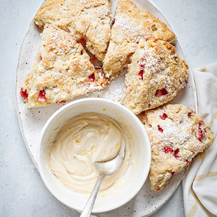 strawberry scones on a white platter with a bowl of lemon glaze
