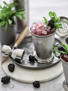 silver julep cup with a blackberry mint julep served on crushed ice and garnished with fresh mint