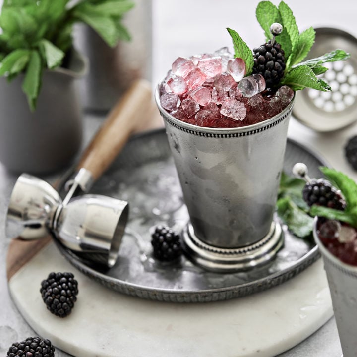 silver julep cup with a blackberry mint julep served on crushed ice and garnished with fresh mint