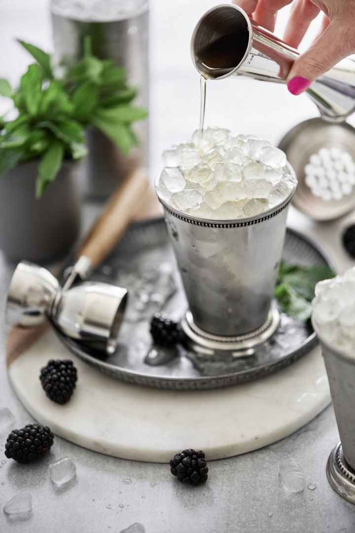 woman pouring bourbon into mint julep cups filled with crushed ice