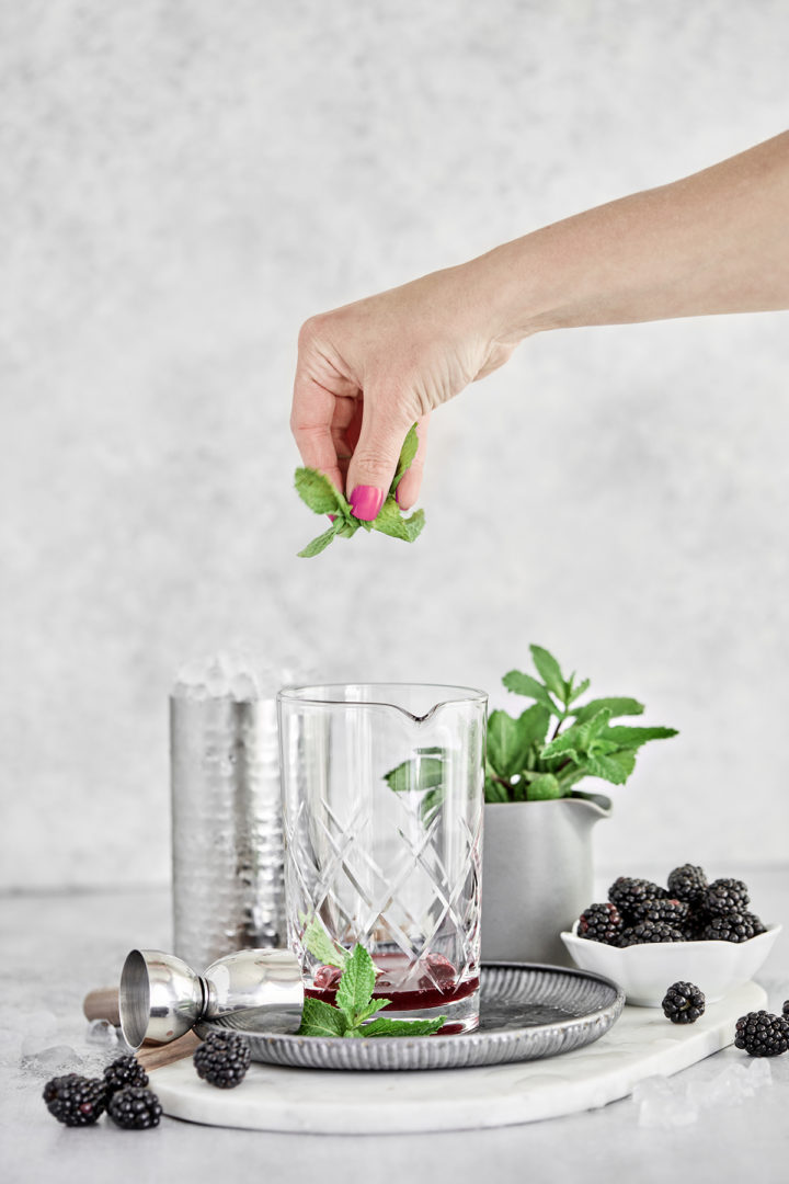 photo of a step showing how to make a mint julep - adding fresh mint to blackberry syrup