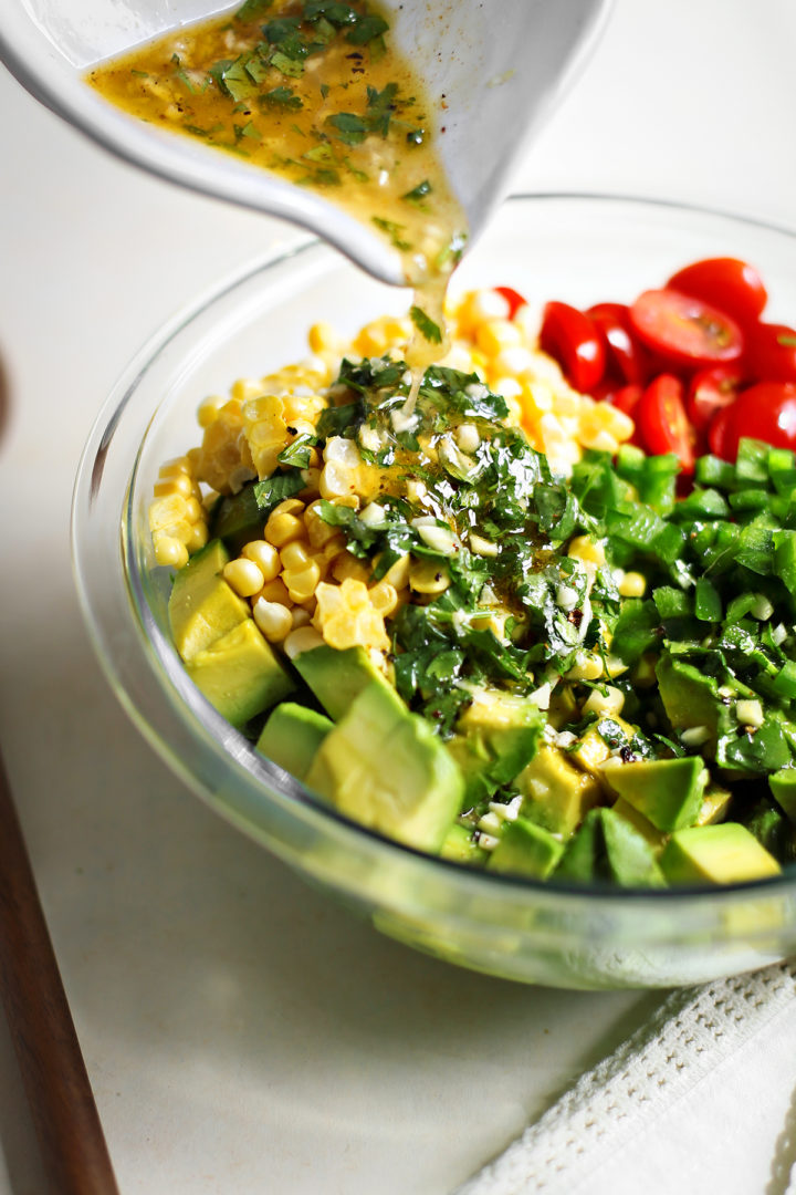 step 3 pouring dressing onto summer corn and tomato salad with avocado