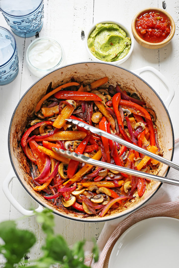 fajita veggies in a cast iron pan on a white wooden table 