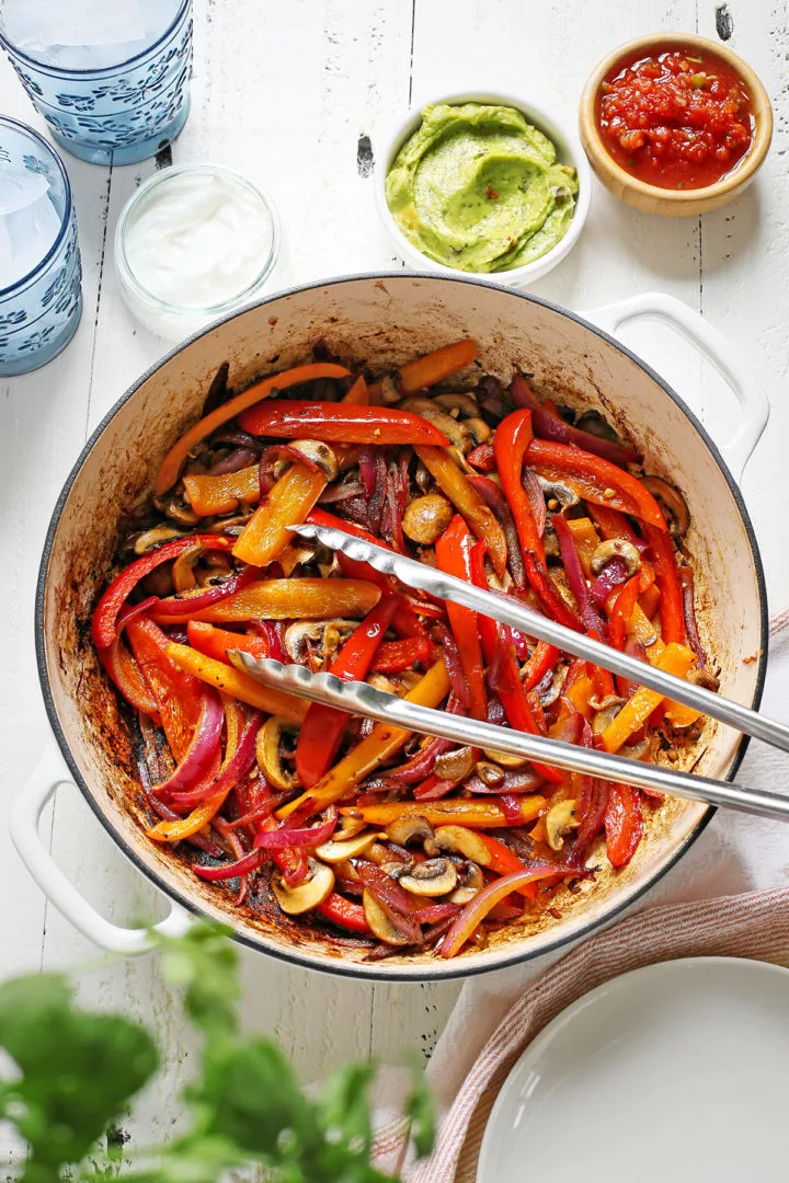 fajita veggies in a cast iron pan on a white wooden table
