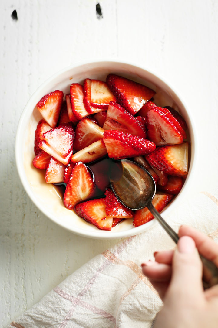 woman stirring sliced strawberries with balsamic vinegar in a white bowl
