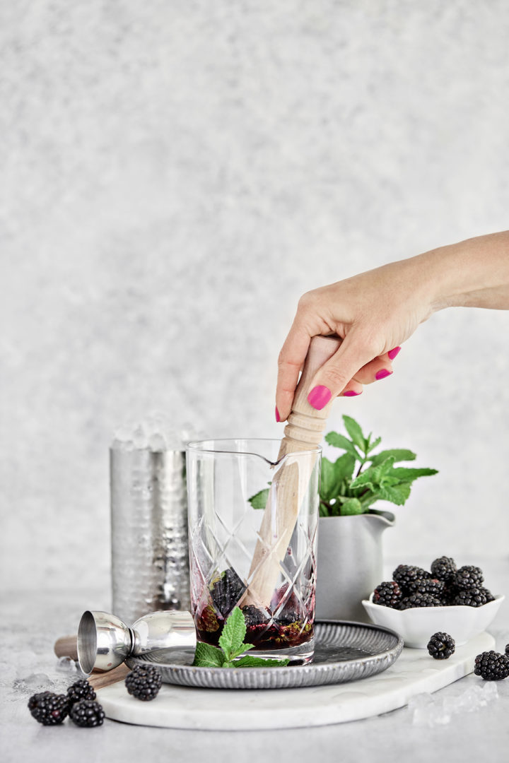 woman muddling fresh blackberries with fresh mint and blackberry simple syrup for making mint juleps