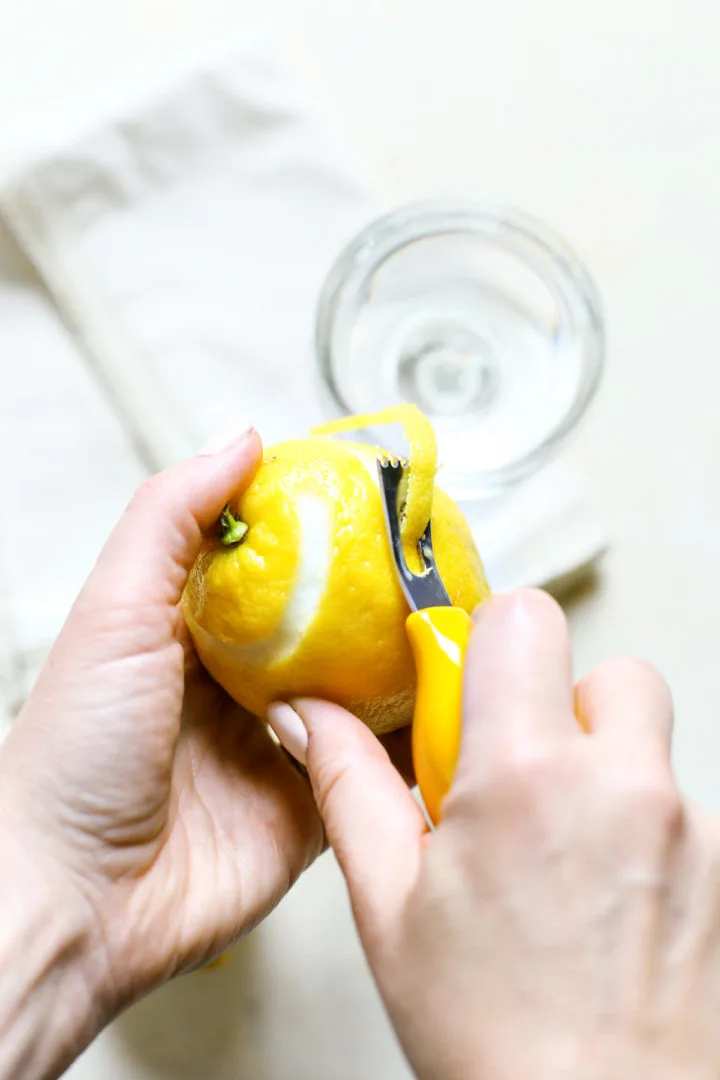 woman using a channel knife to peel a lemon to make a lemon twist garnish