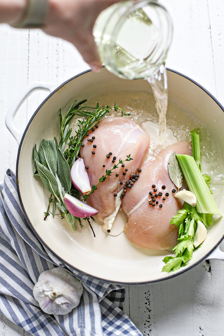 photo showing how to poach chicken	- woman pouring liquid into the poaching pot with chicken and fresh herbs