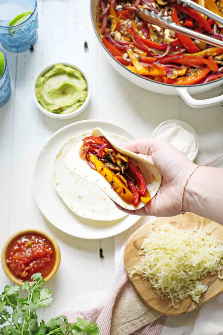 woman assembling her tortilla for this vegetable fajita recipe