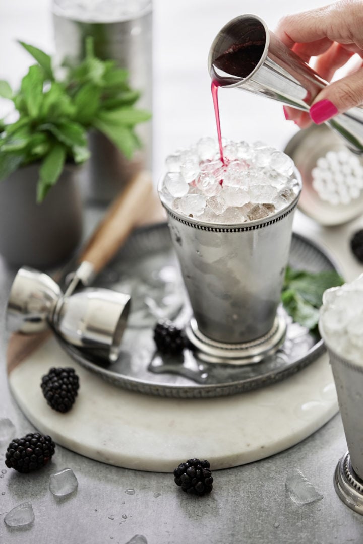 woman adding blackberry simple syrup to a julep cup with ice in it to make a blackberry bourbon cocktail