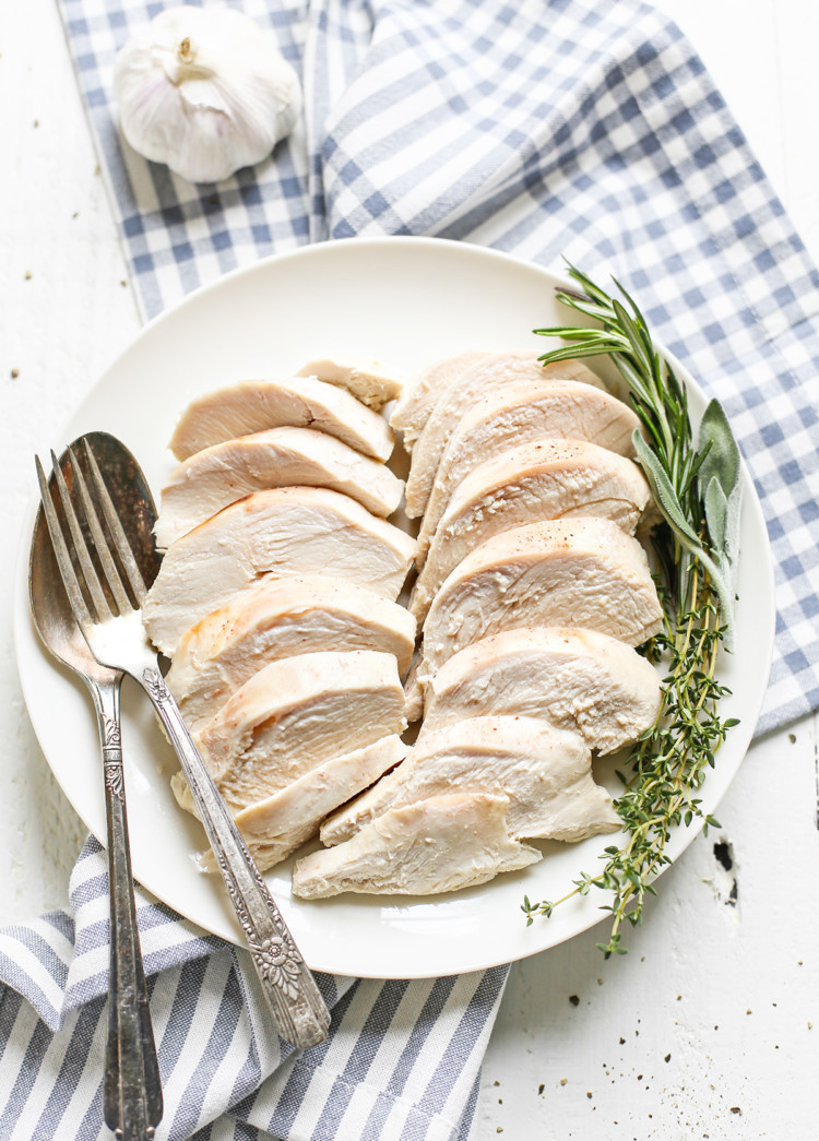 poached chicken on a white plate with fresh herbs