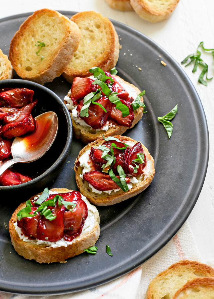 photo of strawberry bruschetta on a black serving plate on a white wooden table