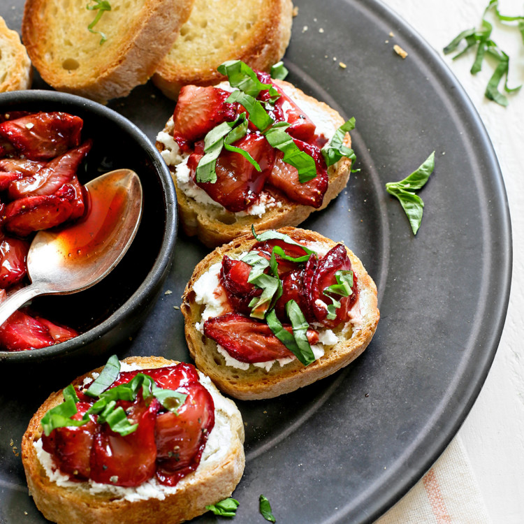 photo of strawberry bruschetta on a black serving plate on a white wooden table