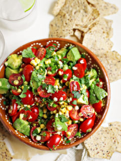 tomato avocado corn salad in a red bowl surrounded by tortilla chips