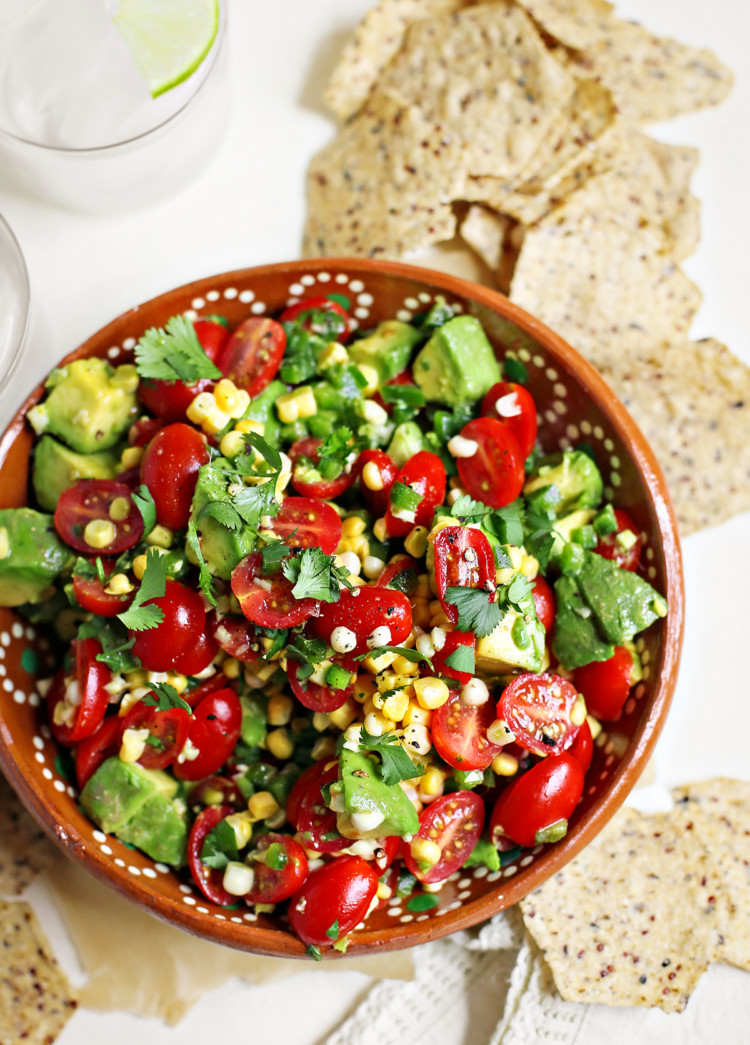 tomato avocado corn salad in a red bowl surrounded by tortilla chips